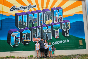 A family standing in front of the Union County mural by Hole in the Wall in Blairsville, Georgia.